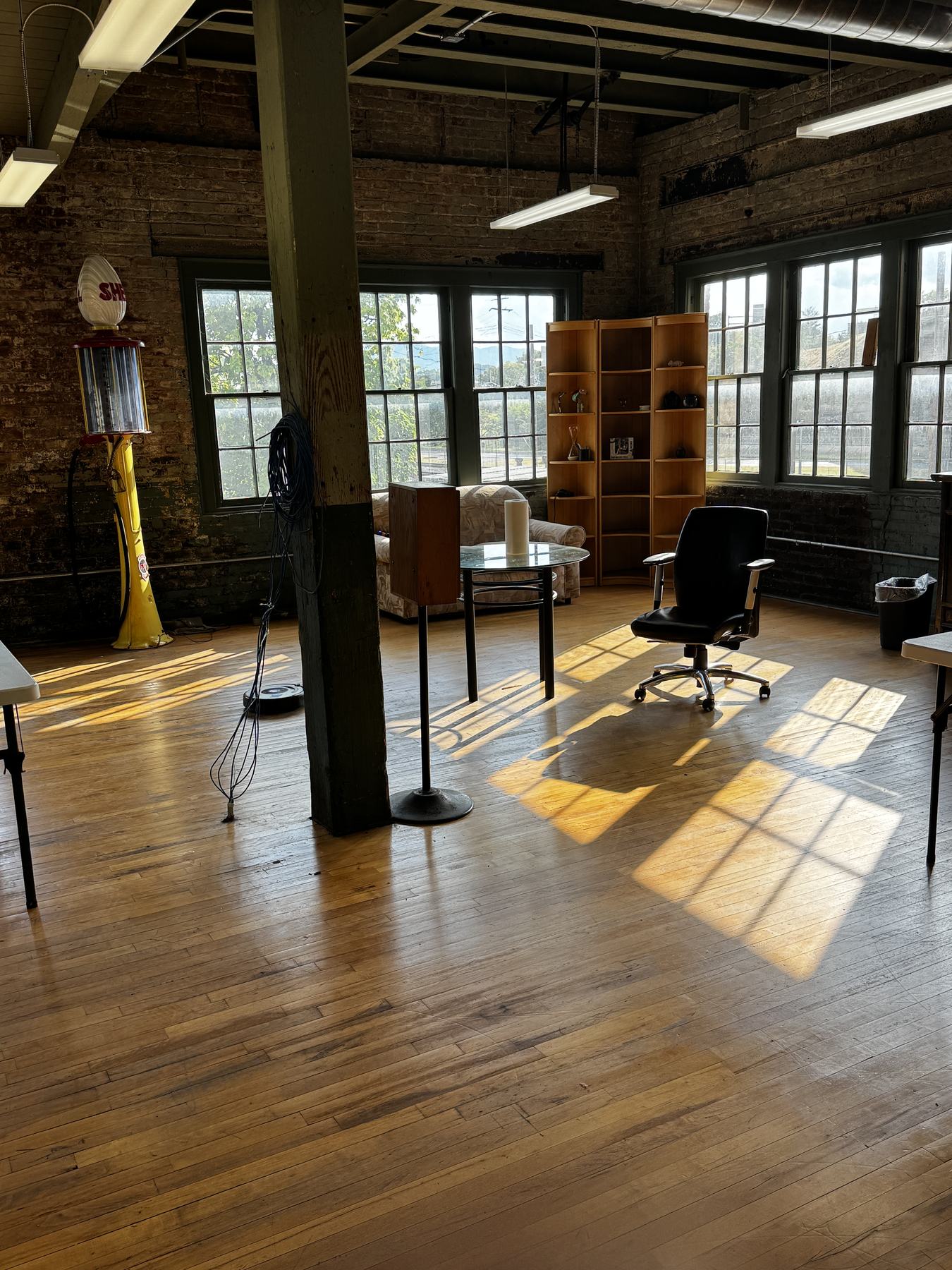 Late sun throwing window-pane shadows across the wood floor, with the lounge corner and a vintage petrol pump against the brick.