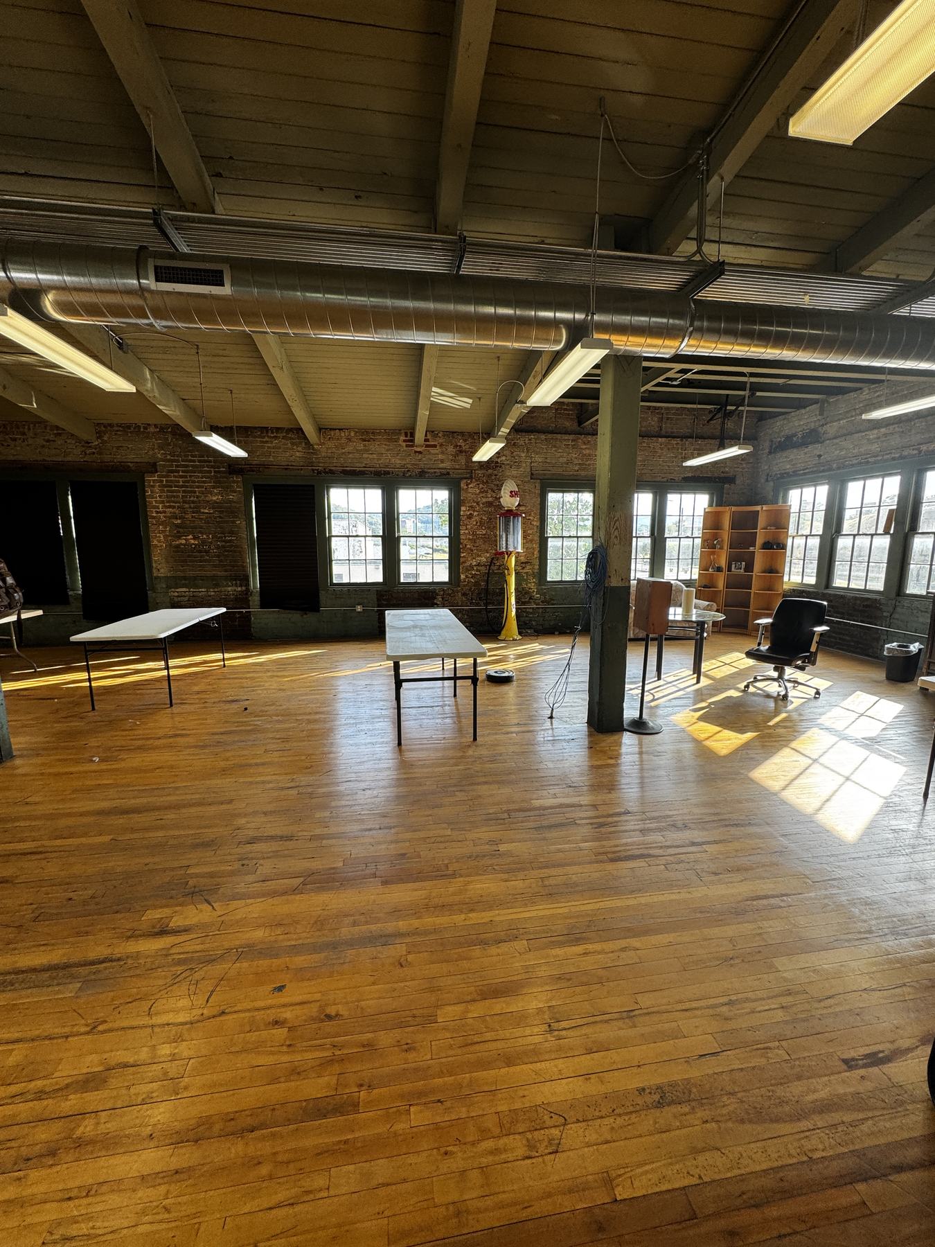 Afternoon light falling across the plank floor from a wall of tall multi-pane windows, with folding tables set out.
